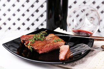 Steak with herbs on plate with wine on wooden background