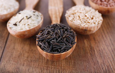Different kinds of rice in spoons on wooden background