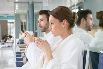 Portrait of couple in bathrobe sitting in relaxation room - obrazy, fototapety, plakaty