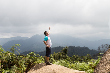 Obraz premium Man standing on the peak of a tropical highland forrest