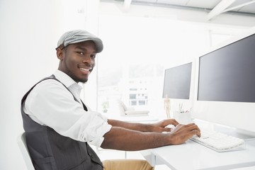 Naklejka na ściany i meble Smiling businessman with hat typing on keyboard