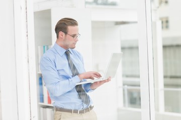 Naklejka na ściany i meble Focused businessman standing and using laptop