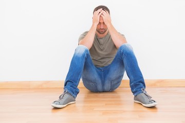 Casual man sitting on floor covering his face at home