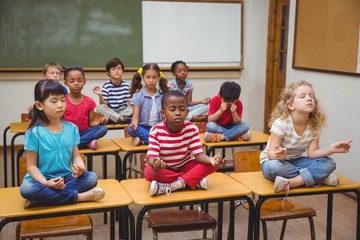 Pupils meditating in lotus position on desk in classroom
