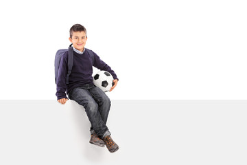 Schoolboy holding soccer ball seated on a panel