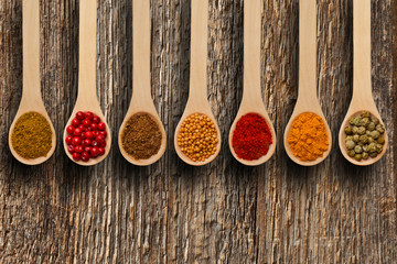 Different spices in the spoons on wooden surface