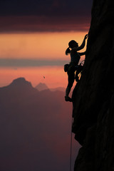 Elegant female alpine climber ascents rock against sunset