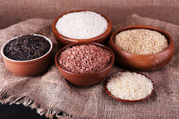 Different kinds of rice in bowls on sackcloth background