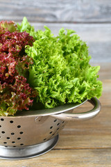 Fresh lettuce in a colander on wooden background