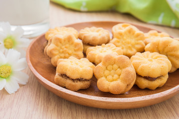 Flower shape biscuits with jam filling on wooden plate