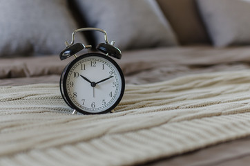 black alarm clock on brown bed with grey pillow