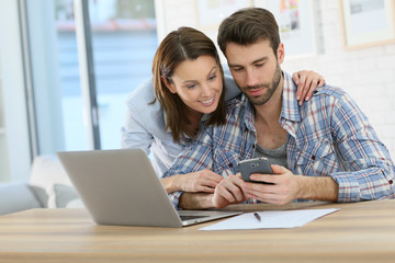 Couple at home using smartphone in front of laptop