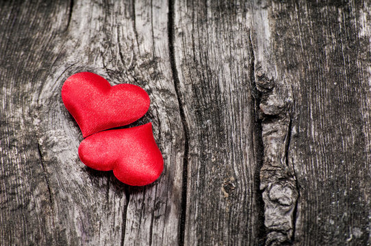 Two satin red hearts on the wooden background