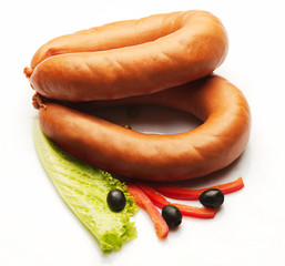 Boiled sausage decorated with red pepper, olive and salad over white background