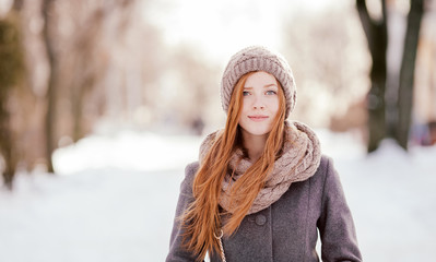Beautiful redhead woman in grey coat strolling in winter park