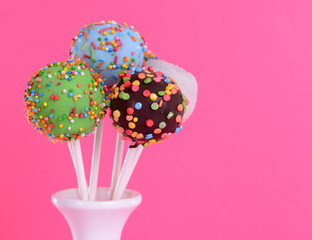 Sweet cake pops in vase on pink background