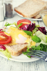 Toast with egg Benedict and tomato on plate on wooden table