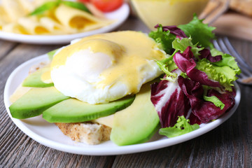 Toast with egg Benedict and avocado on plate on wooden table