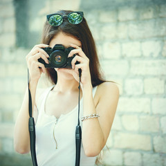 Brunette woman in t-shirt posing with a photo camera outdoors