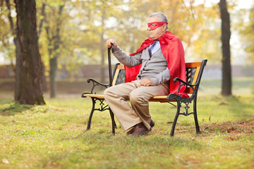 Sad senior in superhero outfit sitting in park
