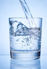 Pouring water into glass on blue background
