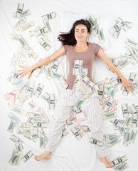 Happy woman sleeping in a bed full of money