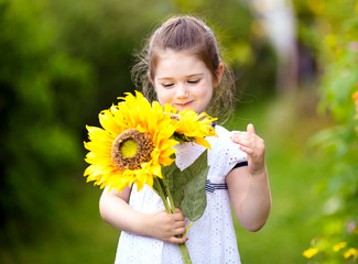 Happy little girl with sunflowers in summer garden