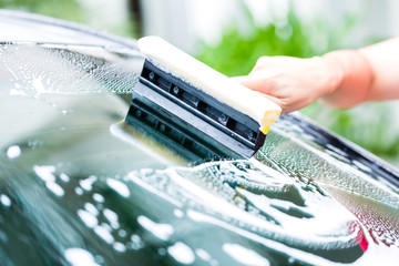 man cleaning windscreen while car wash