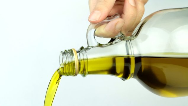 Pouring extra virgin olive oil from glass bottle.  Close up.