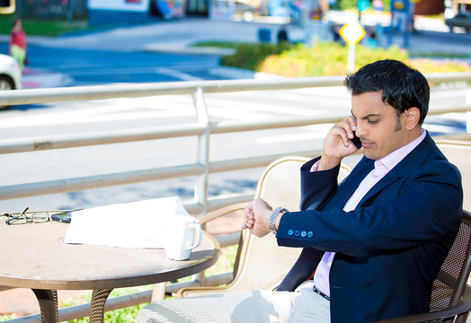 Young business talking on mobile phone looking at his watch