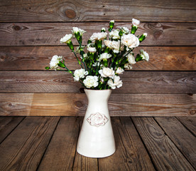 delicate bouquet of carnations in a vase on a vintage wooden bac