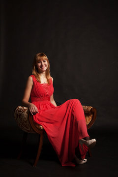 Young Beautiful Woman In Red Dress Sitting On A Chair