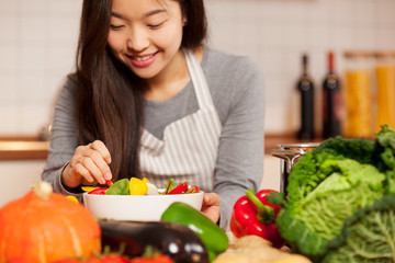 asian smiling woman is composing a colorful salad