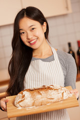 Smiling asian woman is holding fresh baked bread on a wooden tra
