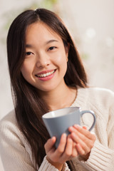 Asian woman with hot mug in her hands smiling towards the camera