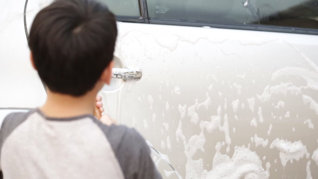Asian cute boy washing car . Child helping family clean big car.