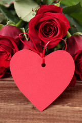 Fototapeta na wymiar Valentine background of gift tag and red roses on wood