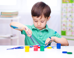 Little boy is playing with paints