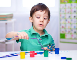 Little boy is playing with paints