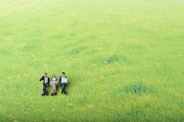 Fototapeta na wymiar 草原の中でパソコンで仕事をしている３人のビジネスマンのミニチュア