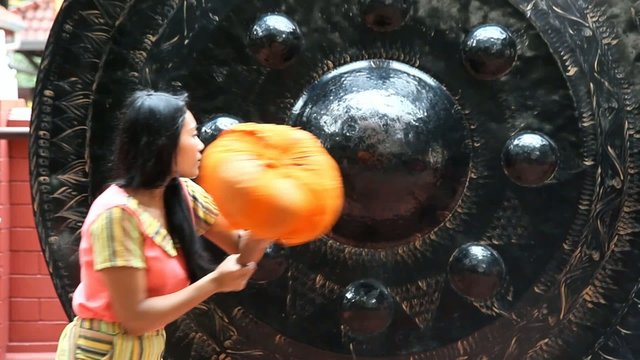 Young woman strikes a gong in a Buddhist temple