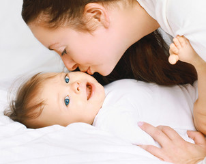 Mom kissing little baby on the bed at home