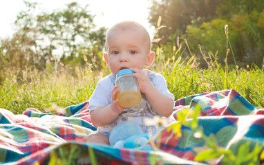 Baby sitting on plaid and drinking juice, summer sunset