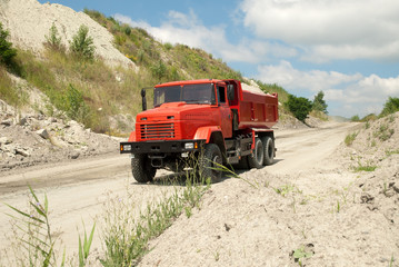 Red dump truck driving on a road in a stone quarry