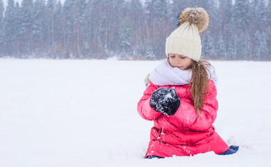 Happy adorable little girl playing snowballs in snowy winter day