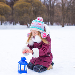 Little girl warms hands on candle in lantern outdoors