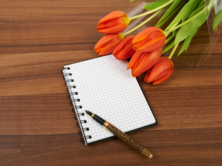 Notebook with tulips on wooden background on a table