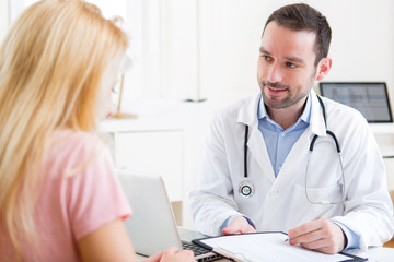 Young attractive doctor taking notes while patient speaking
