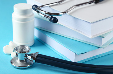 Medical stethoscope with books and tablet on blue background