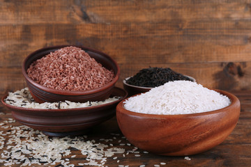 Different kinds of rice in bowls on wooden background